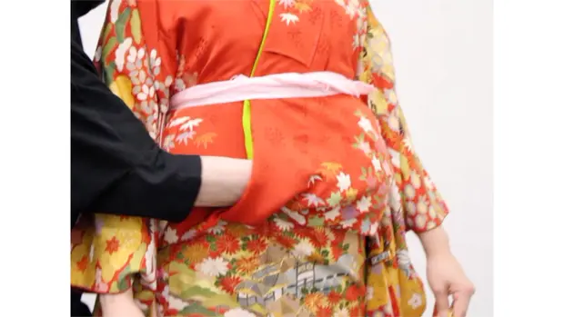 下前を引いて振袖のおはしょりのたるみを取る